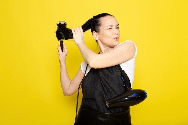 Foto gratuita un giovane parrucchiere femminile di vista frontale in mantello nero della maglietta bianca che spazzola la sua posa sorridente dei capelli