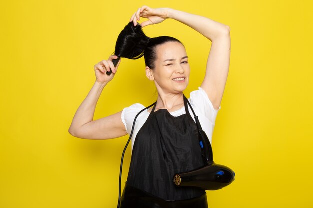 A front view young female hairdresser in white t-shirt black cape brushing her hair smiling posing