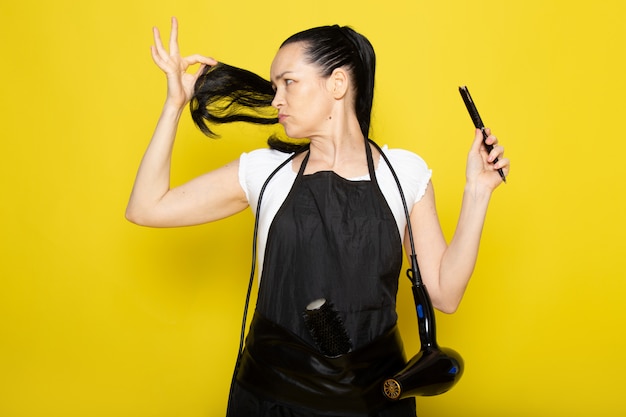 Foto gratuita un giovane parrucchiere femminile di vista frontale in mantello nero della maglietta bianca che taglia la sua posa dei capelli