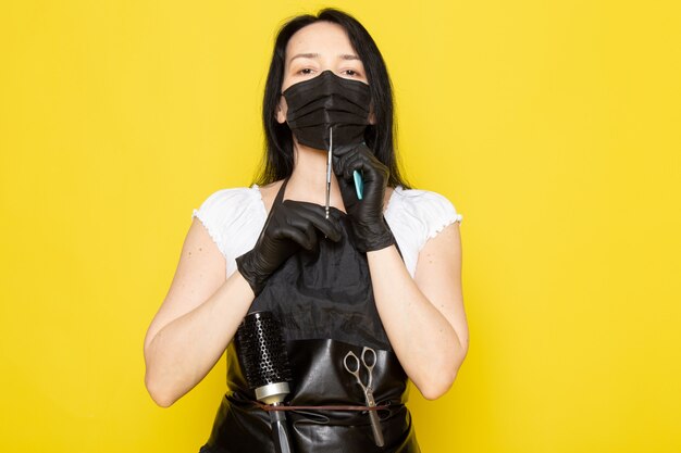 黒の滅菌マスク黒手袋ではさみを保持している白いtシャツ黒ケープの正面の若い女性美容師