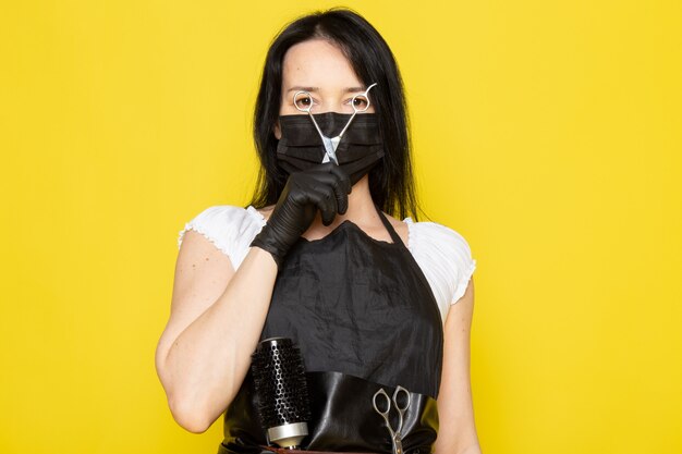 黒の滅菌マスク黒手袋ではさみを保持している白いtシャツ黒ケープの正面の若い女性美容師