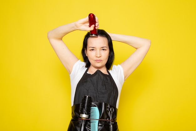 A front view young female hairdresser in white t-shirt black cape using mechanical hair machine wave hair