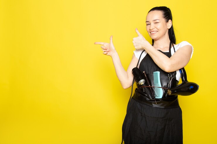 無料Photo ブラシとドライヤー歓迎のポーズを笑顔で白いtシャツブラックケープの正面の若い女性美容師