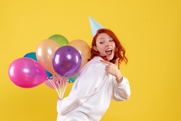 Front view young female hiding cute colorful balloons on yellow 