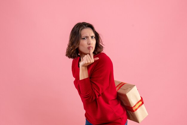 Front view young female hiding xmas present behind her back on the pink 