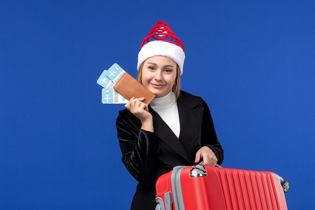 青い壁の飛行機の休日の旅行でバッグと飛行機のチケットを保持している若い女性の正面図