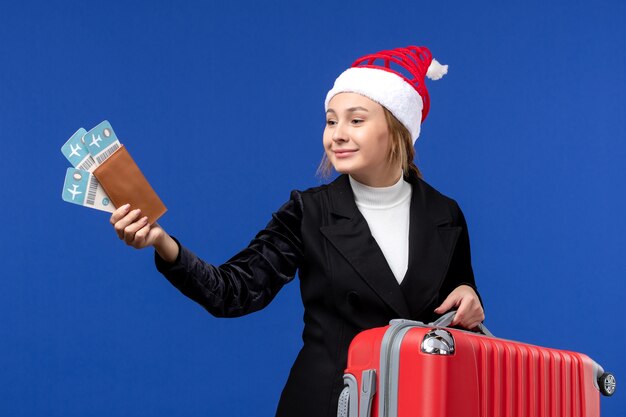 青い壁の飛行機の休日の休暇でバッグとチケットを保持している若い女性の正面図