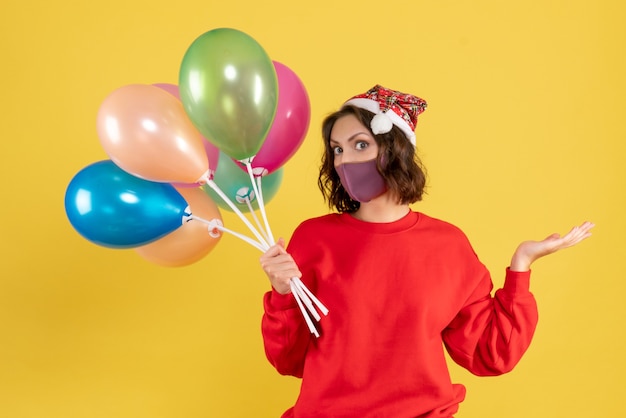 Front view young female holding balloons in sterile mask on yellow desk new year color woman emotion party celebration