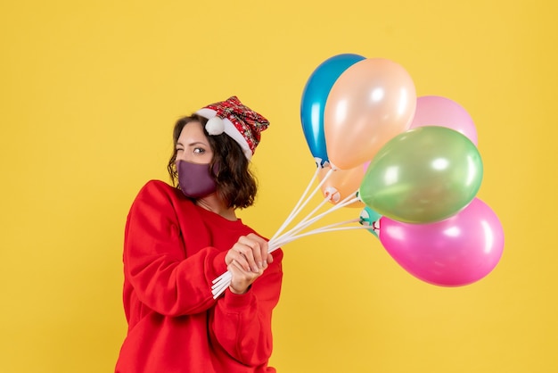 Front view young female holding balloons in sterile mask on a yellow 