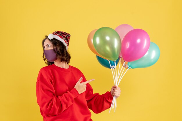 Вид спереди молодая женщина, держащая воздушные шары в стерильной маске на желтом