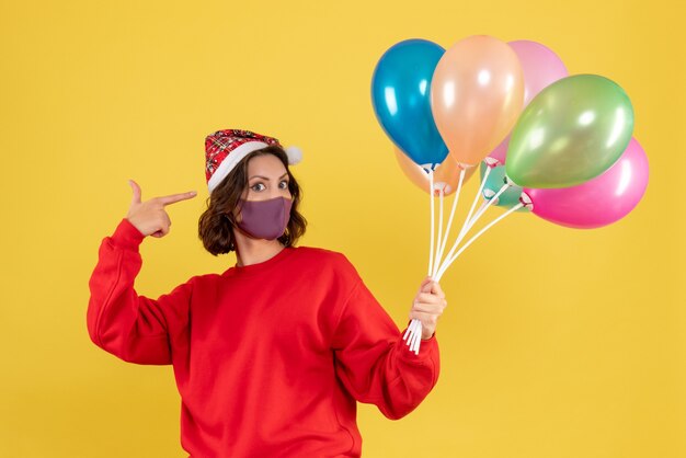 Front view young female holding balloons in sterile mask on yellow 