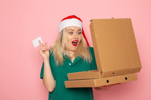 Бесплатное фото Вид спереди молодая женщина, держащая банковскую карту и коробки для пиццы на розовой стене, праздничная рождественская новогодняя фото-форма