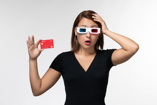 Front view young female holding bank card in d sunglasses and thinking on white surface