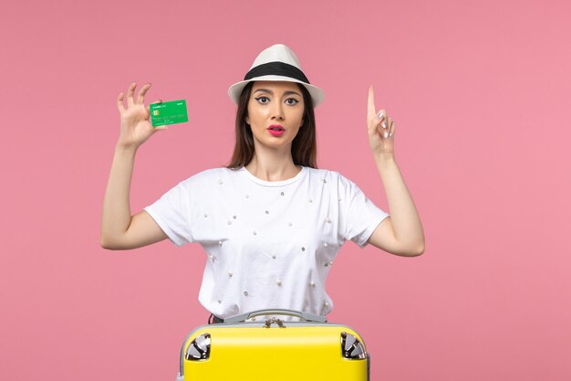 淡いピンクの壁の感情の夏の女性の旅行で銀行カードを保持している若い女性の正面図
