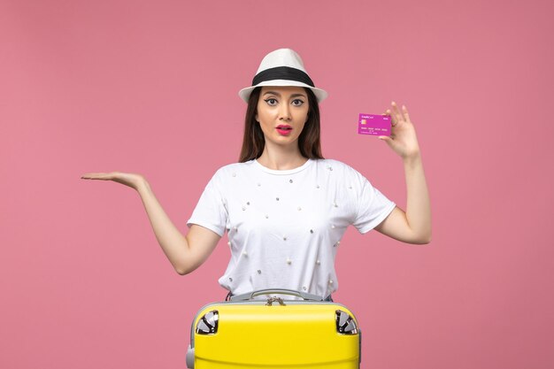 Вид спереди молодая женщина, держащая банковскую карту на светло-розовой стене, поездка, женщина, отпуск, деньги