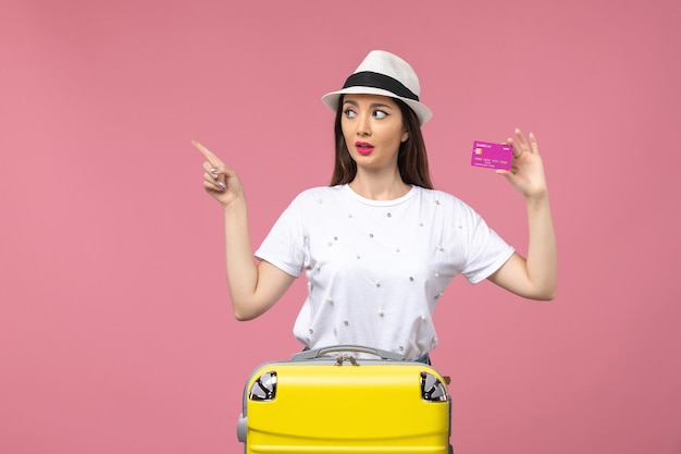 Front view young female holding bank card on light pink wall trip woman vacation money