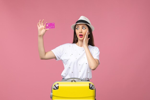ピンクのデスク旅行お金の色の休暇で銀行カードを保持している若い女性の正面図
