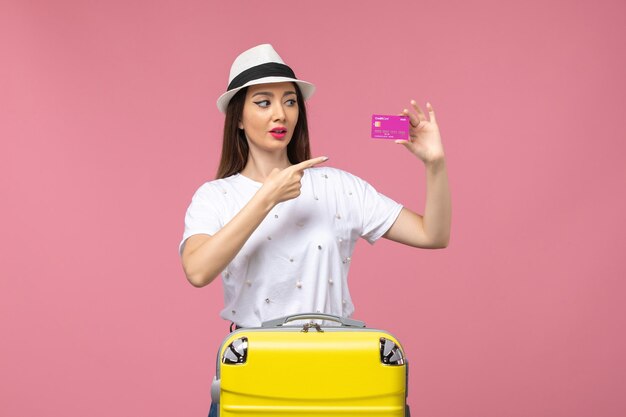 ピンクのデスク旅行の女性の休暇のお金で銀行カードを保持している正面図若い女性