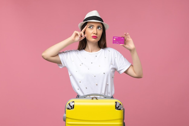 ピンクの壁の休暇の女性の旅行のお金で銀行カードを保持している正面図若い女性