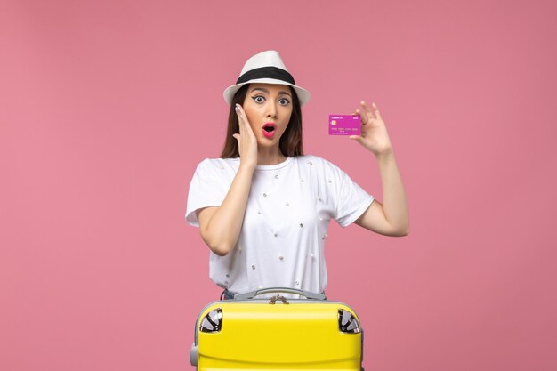 ピンクの壁の女性の休暇のお金の旅で銀行カードを保持している若い女性の正面図