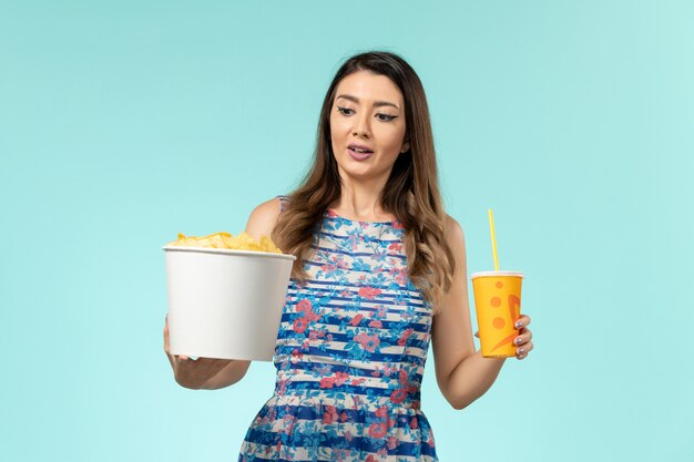 Front view young female holding basket with chips and drink on blue desk