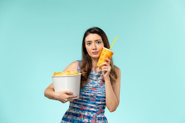 Front view young female holding basket with chips and drink on blue surface