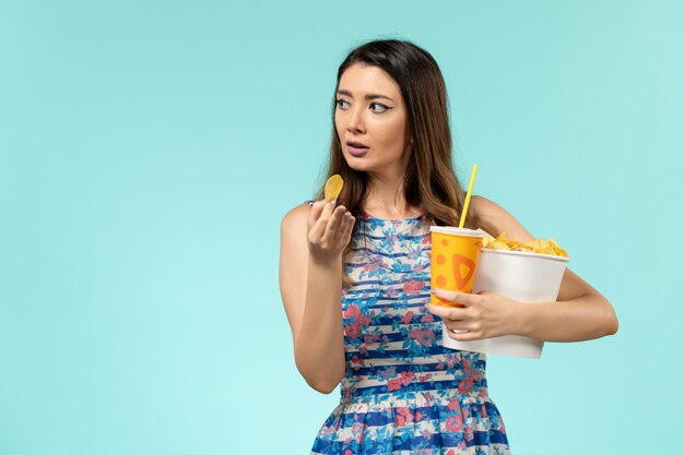 Front view young female holding basket with chips and drink on light-blue surface