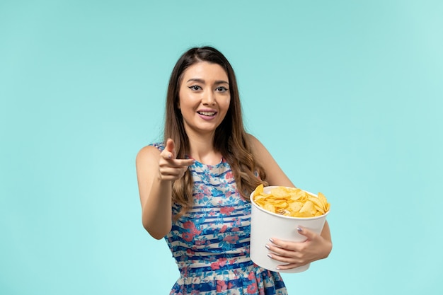 Free photo front view young female holding basket with chips laughing on blue surface