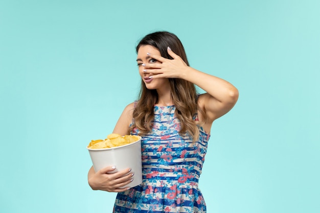 Front view young female holding basket with chips and watching movie on the blue surface