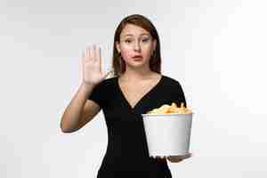 Free photo front view young female holding basket with potato chips and watching movie on white desk