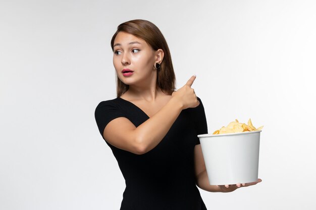 Вид спереди молодая женщина, держащая корзину с картофельными чипсами, смотрит фильм на белом столе