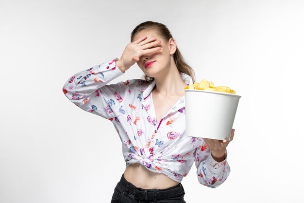 Вид спереди молодая женщина, держащая корзину с картофельными чипсами, смотрит фильм на белой поверхности
