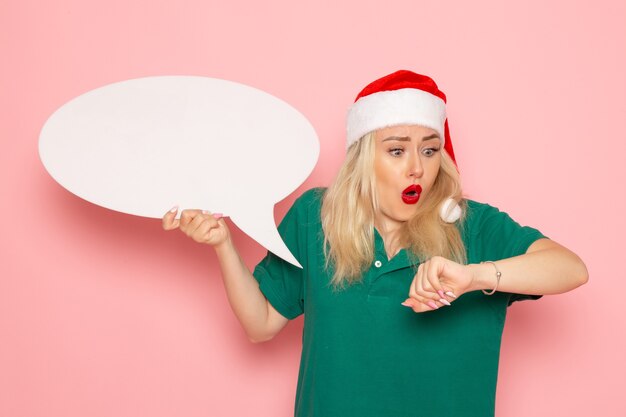 Foto gratuita giovane femmina di vista frontale che tiene grande segno bianco che controlla tempo sulla donna di festa di capodanno della foto della neve della parete rosa