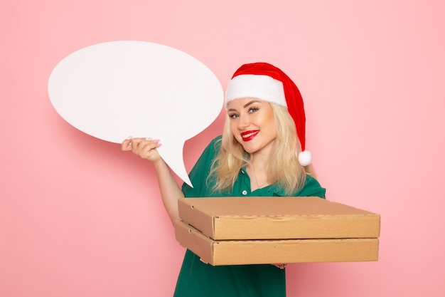 Vista frontale giovane femmina che tiene grande cartello bianco e scatole di cibo su una parete rosa foto lavoro capodanno vacanza lavoro corriere uniforme