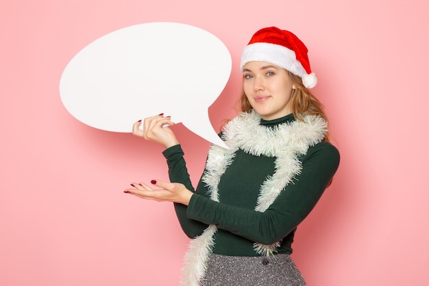 Free photo front view young female holding big white sign on pink wall christmas new year model holiday color emotion