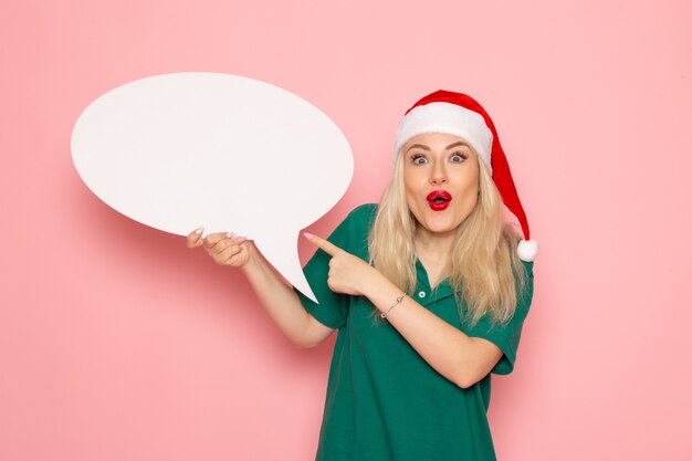 Free photo front view young female holding big white sign on a pink wall woman snow color photo new year holiday