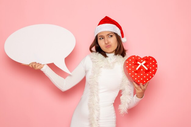 Front view young female holding big white sign and present on pink wall emotion color snow christmas new year holidays