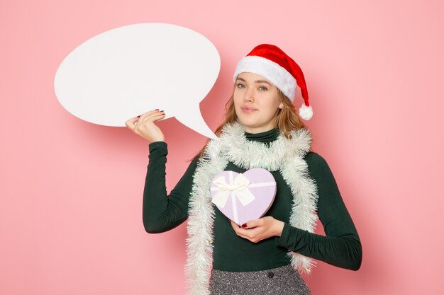 Free photo front view young female holding big white sign and present on pink wall model christmas new year holidays color emotion