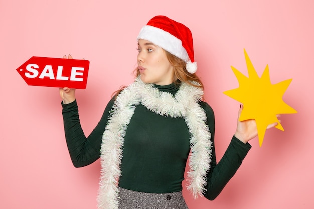 Free photo front view young female holding big yellow figure and sale writing on pink wall color model holiday christmas new year emotion