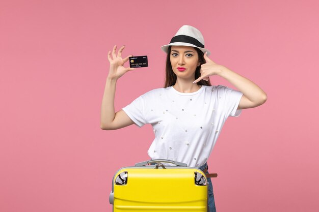 Front view young female holding black bank card on a pink wall voyage summer trip