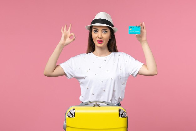 Front view young female holding blue bank card on light pink wall color trip voyage