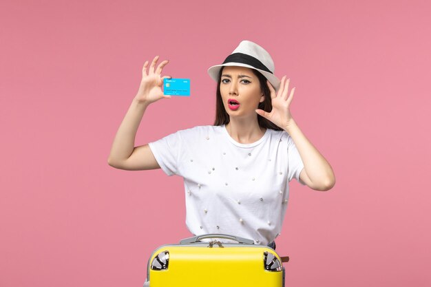 Вид спереди молодая женщина, держащая синюю банковскую карту на светло-розовой стене, цветная поездка, лето