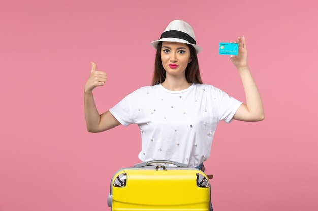 Front view young female holding blue bank card on the pink wall color trip voyage