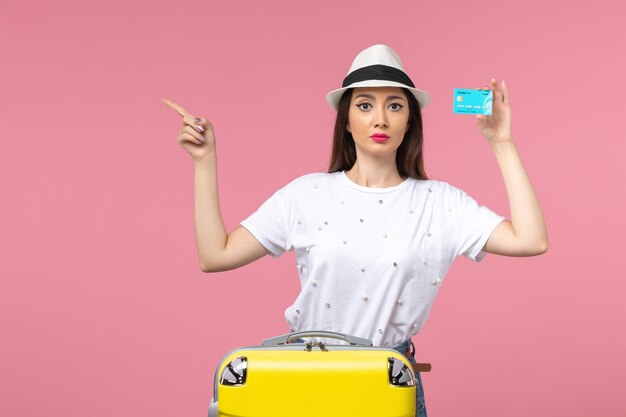 Front view young female holding blue bank card on pink wall trip color voyage