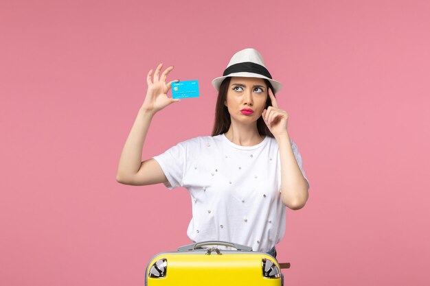 Front view young female holding blue bank card on a pink wall voyage trip summer