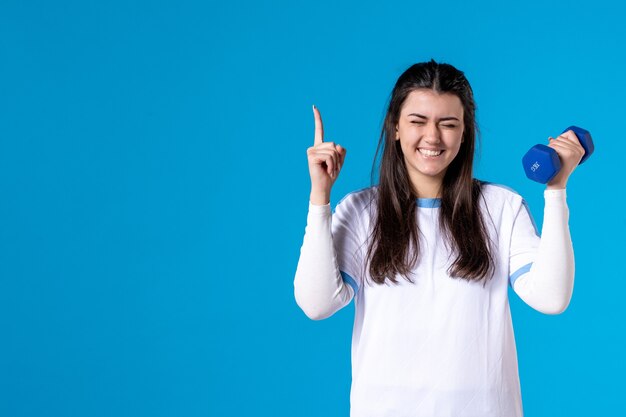 Front view young female holding blue dumbbells on blue wall