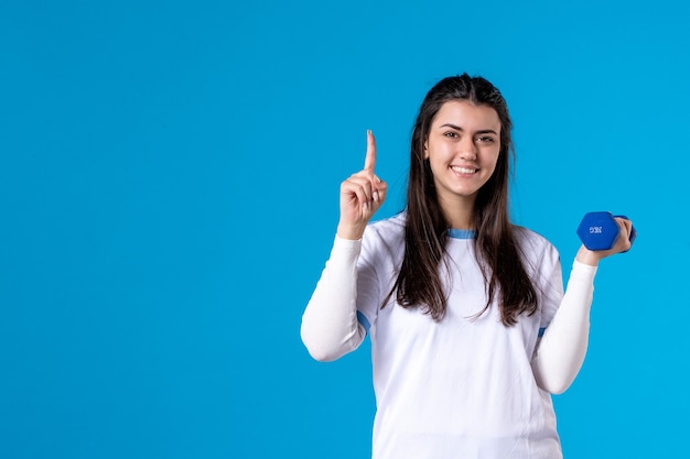 Front view young female holding blue dumbbells on blue wall