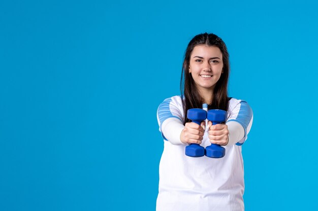 Front view young female holding blue dumbbells on blue wall