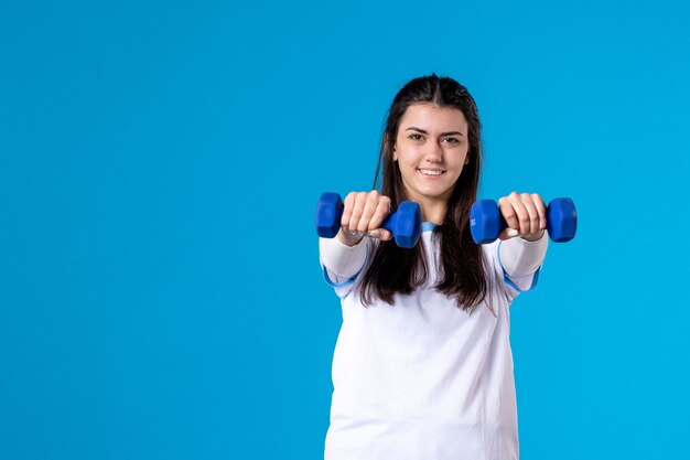 Front view young female holding blue dumbbells on blue wall