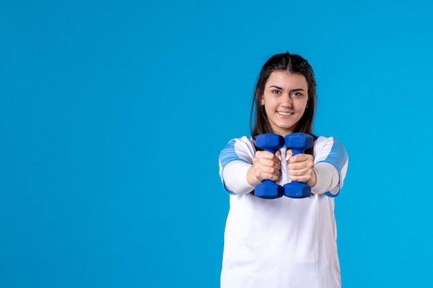 Front view young female holding blue dumbbells on blue wall